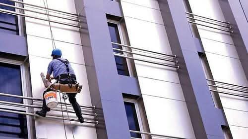Pintor trabalhando com segurança na fachada de um prédio